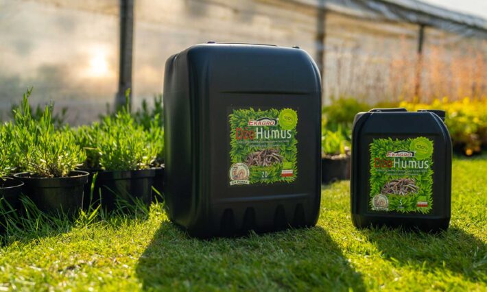 Płynny DżoHumus Ekagro w kanistrach ustawionych w ogrodzie przy sadzonkach – naturalny biohumus do nawożenia roślin doniczkowych i ogrodowych