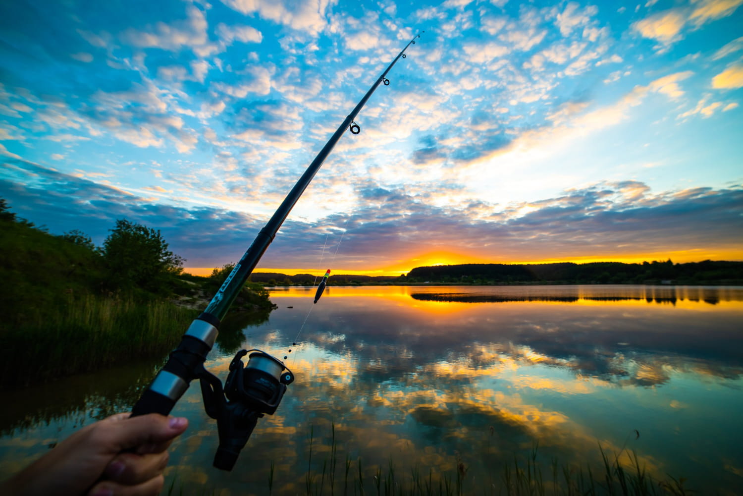 Wędka z kołowrotkiem podczas połowu nad jeziorem o zachodzie słońca